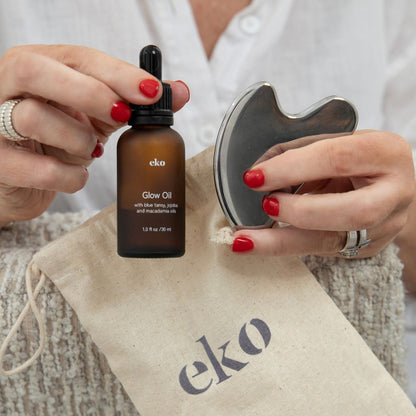 Person holding a bottle of eko Glow Oil with a pouch and roller in the background